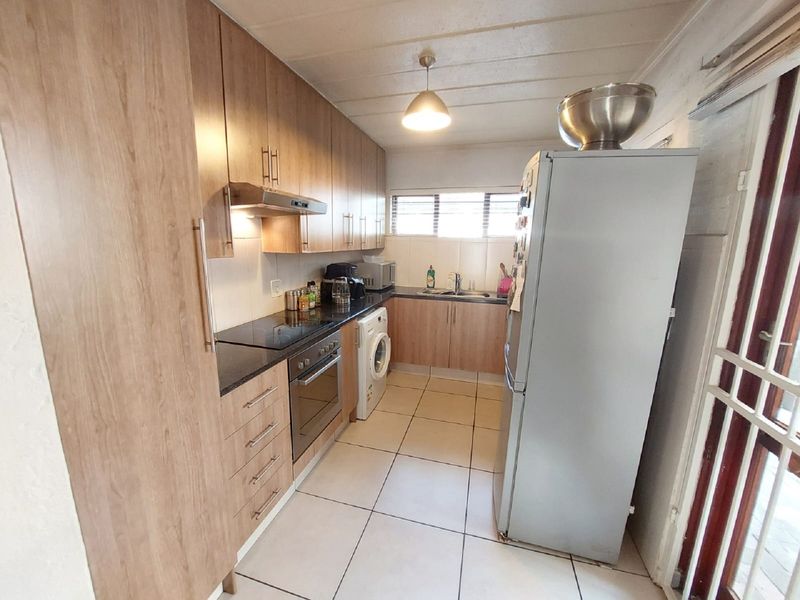 A functional galley-style kitchen featuring wood-finish cabinetry, dark countertops, integrated appliances, and tiled flooring with direct access to an outdoor area.