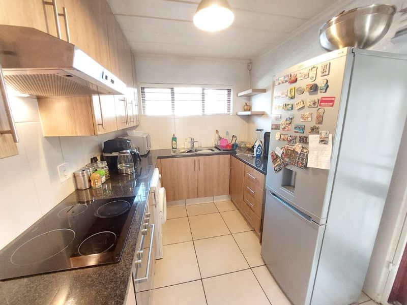 A functional kitchen featuring wood-finish cabinetry, granite countertops, an electric hob with extractor fan, and tiled flooring.
