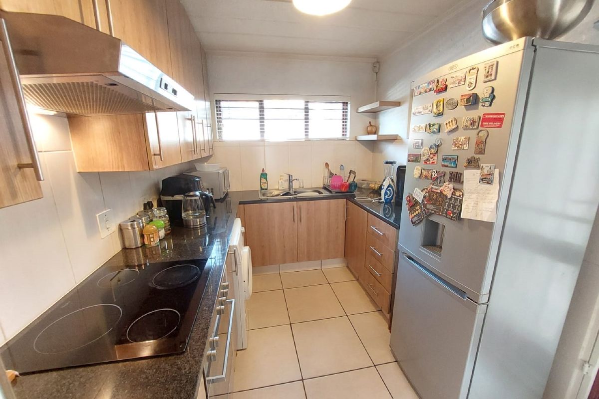 A functional galley-style kitchen featuring light wood-finish cabinetry, dark granite countertops, an electric hob with extractor, and tiled flooring.