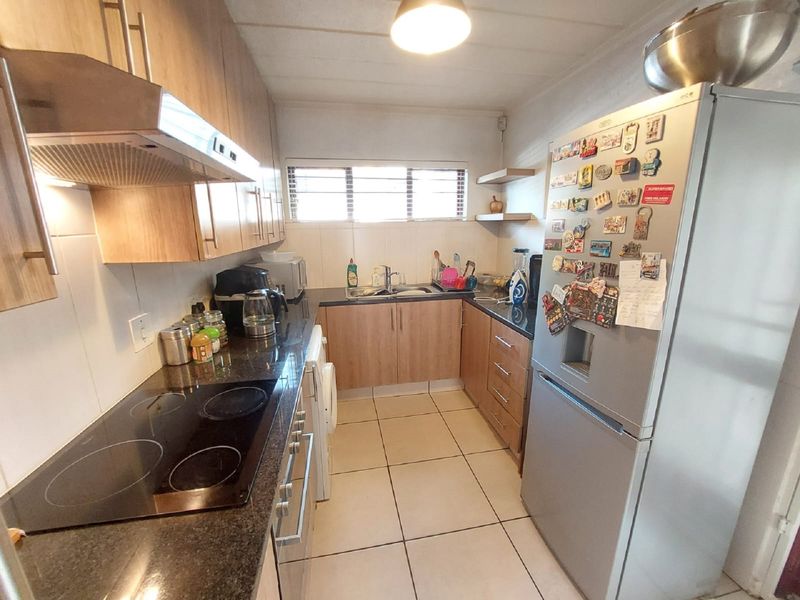 A functional galley-style kitchen featuring light wood-finish cabinetry, dark granite countertops, an electric hob with extractor, and tiled flooring.