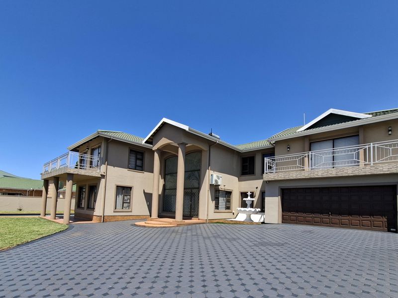 A spacious double-story residence featuring a large paved driveway, double garage, upper-level balconies with metal railings, and a decorative fountain in the front garden.