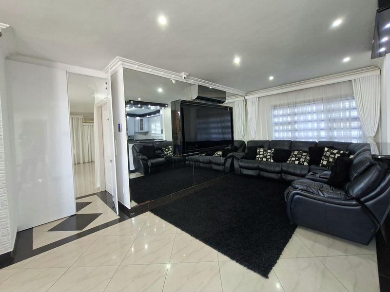 Spacious living room featuring tiled flooring, recessed downlighting, decorative ceiling cornices, and a large mirrored feature wall with integrated air conditioning.