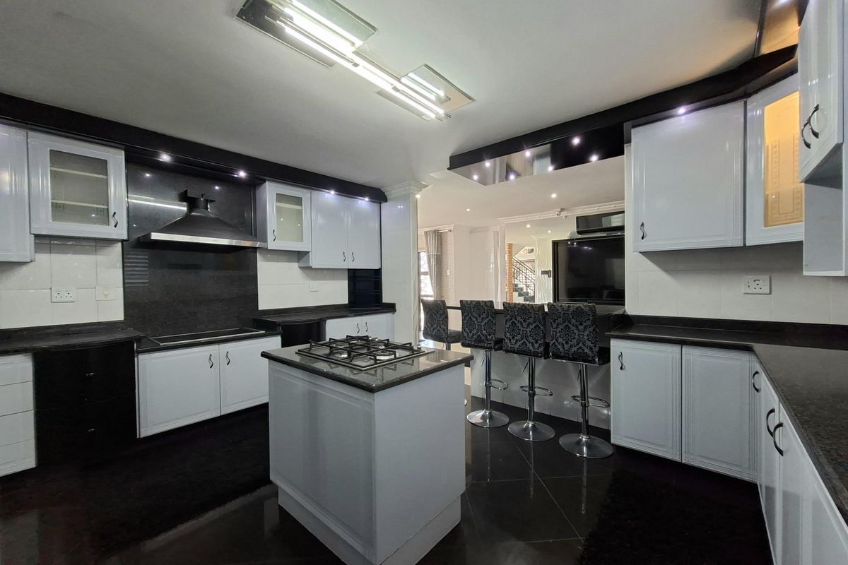 Modern kitchen featuring a central island with gas hob, high-contrast cabinetry, granite countertops, and integrated lighting, flowing into an open-plan living area.