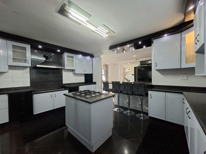 Modern kitchen featuring a central island with gas hob, high-contrast cabinetry, granite countertops, and integrated lighting, flowing into an open-plan living area.