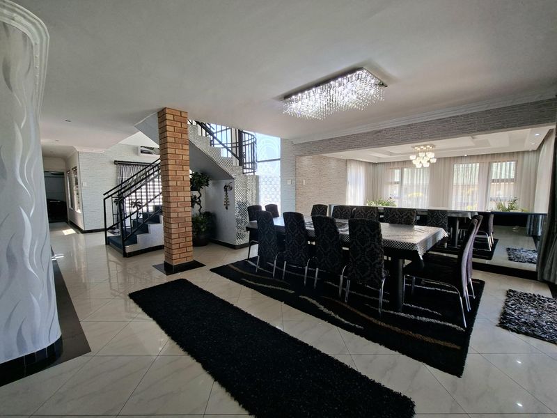 Spacious open-plan dining area featuring elegant crystal lighting, polished porcelain flooring, a striking exposed brick pillar, and a feature staircase.