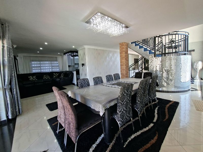 Spacious open-plan living and dining area featuring a striking crystal chandelier, decorative mirrored wall, and a prominent staircase with wrought iron balustrades.
