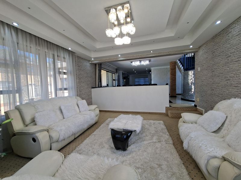 Spacious living room featuring a recessed ceiling with modern chandelier lighting, textured stone wall cladding, and an integrated staircase.