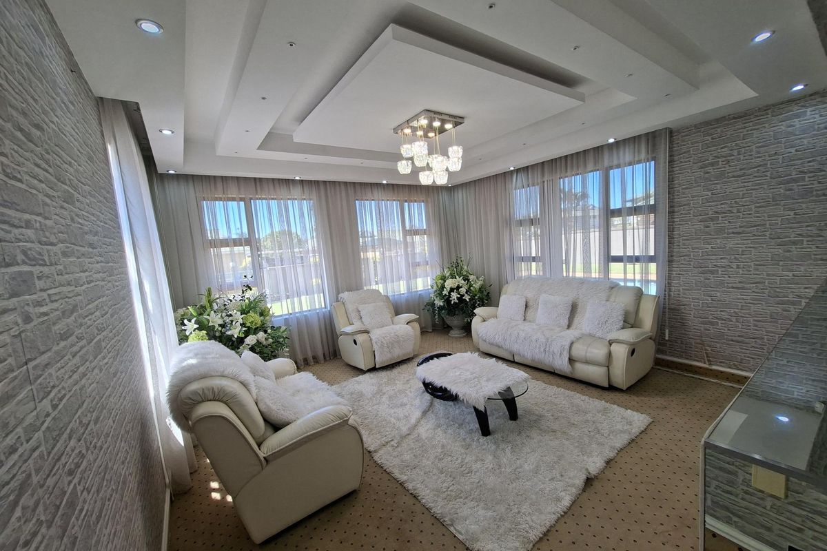 A bright and well-maintained living room featuring a sophisticated coffered ceiling with recessed lighting, a modern chandelier, and large windows with textured wall finishes.