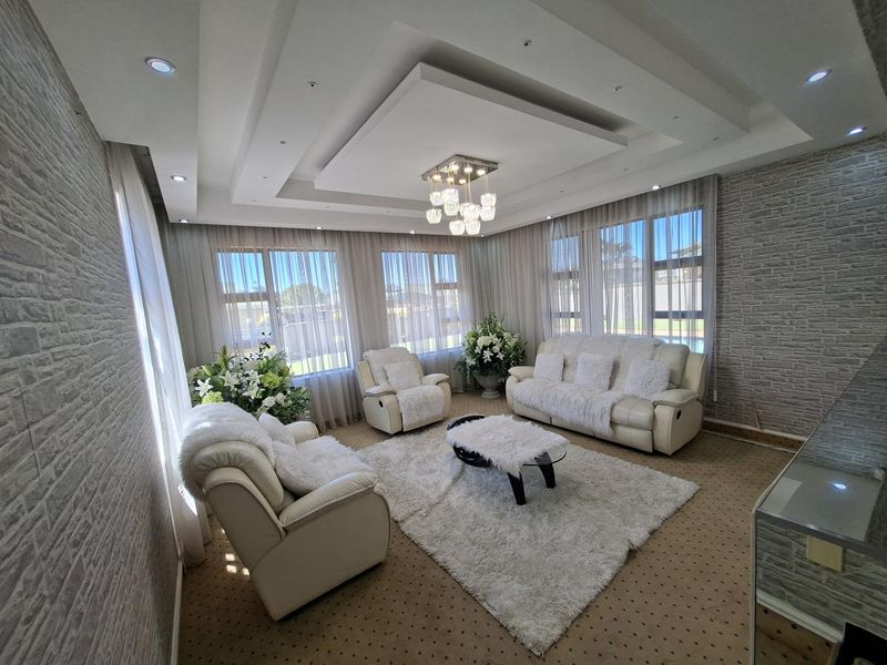 A bright and well-maintained living room featuring a sophisticated coffered ceiling with recessed lighting, a modern chandelier, and large windows with textured wall finishes.