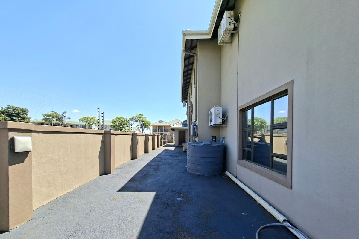 A side exterior view of the property featuring a paved pathway, boundary wall, water tank, and wall-mounted air conditioning units.