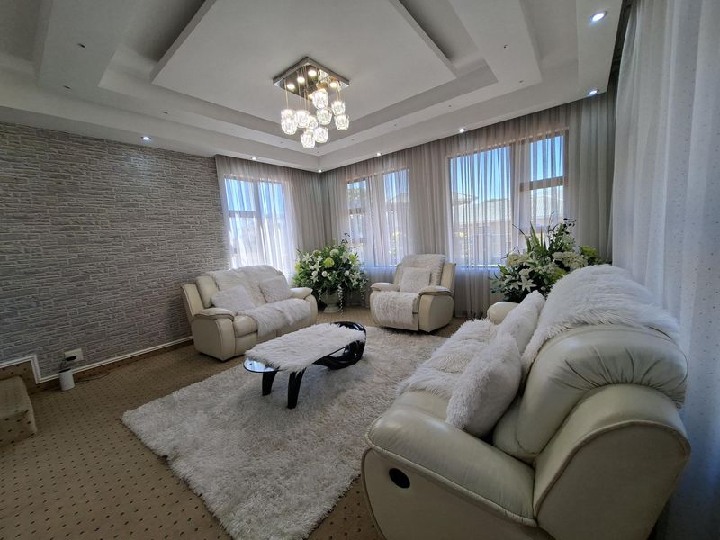 A well-lit living room featuring a decorative stone accent wall, recessed ceiling with modern lighting, and large windows with sheer curtains.