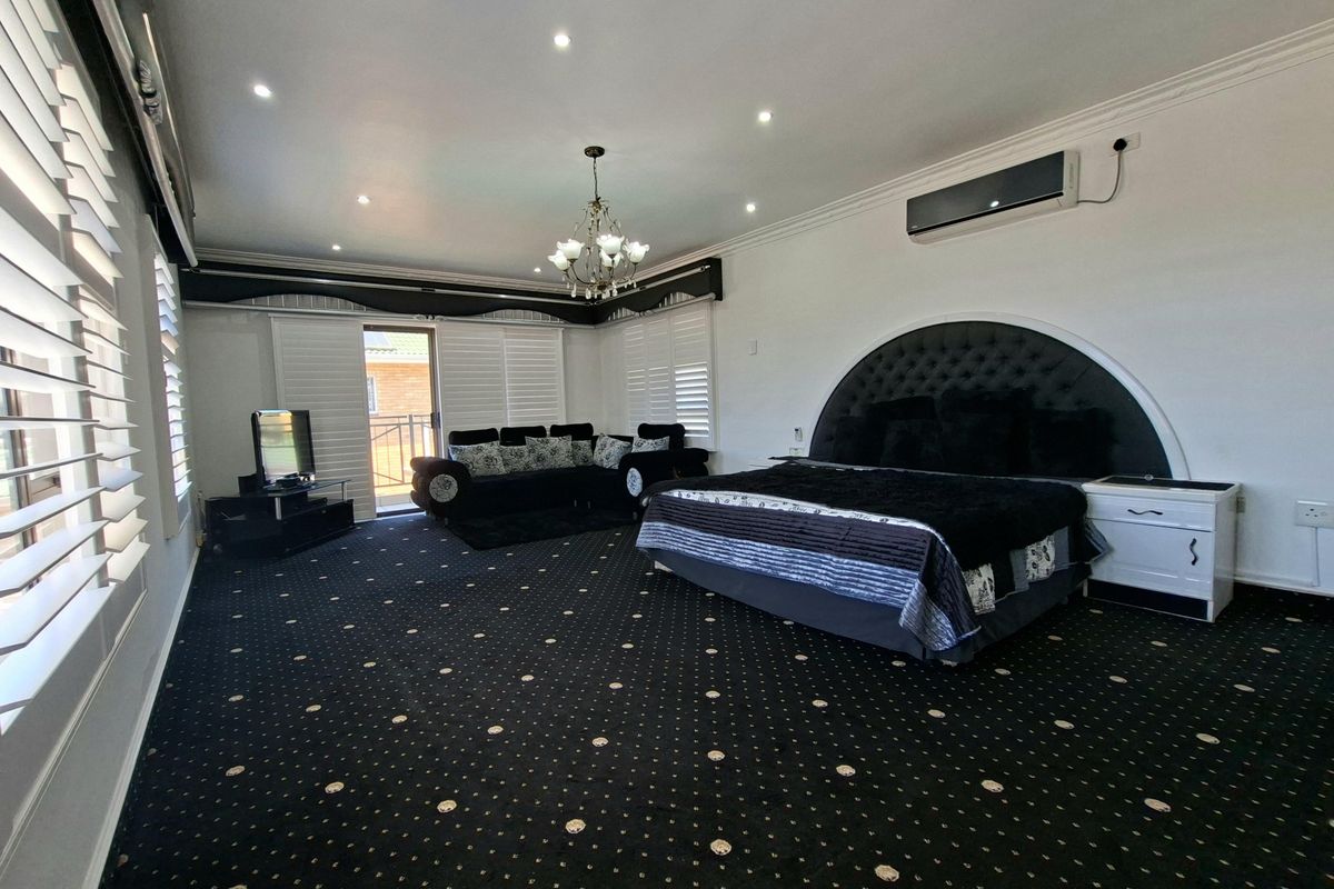 Spacious bedroom featuring recessed downlights, split-system air conditioning, and plantation shutters, with direct access to an outdoor area via a sliding glass door.