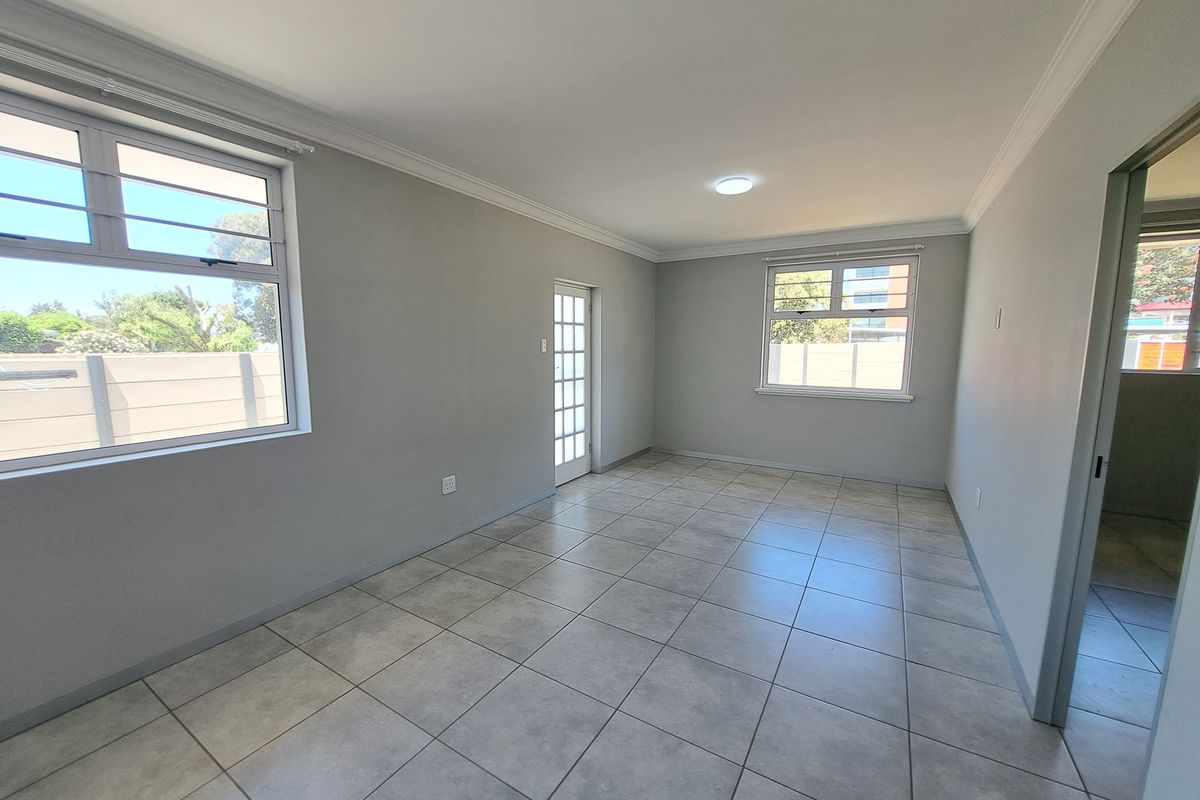A bright, empty living area featuring neutral grey walls, tiled flooring, and a glass-paneled door leading to the exterior.