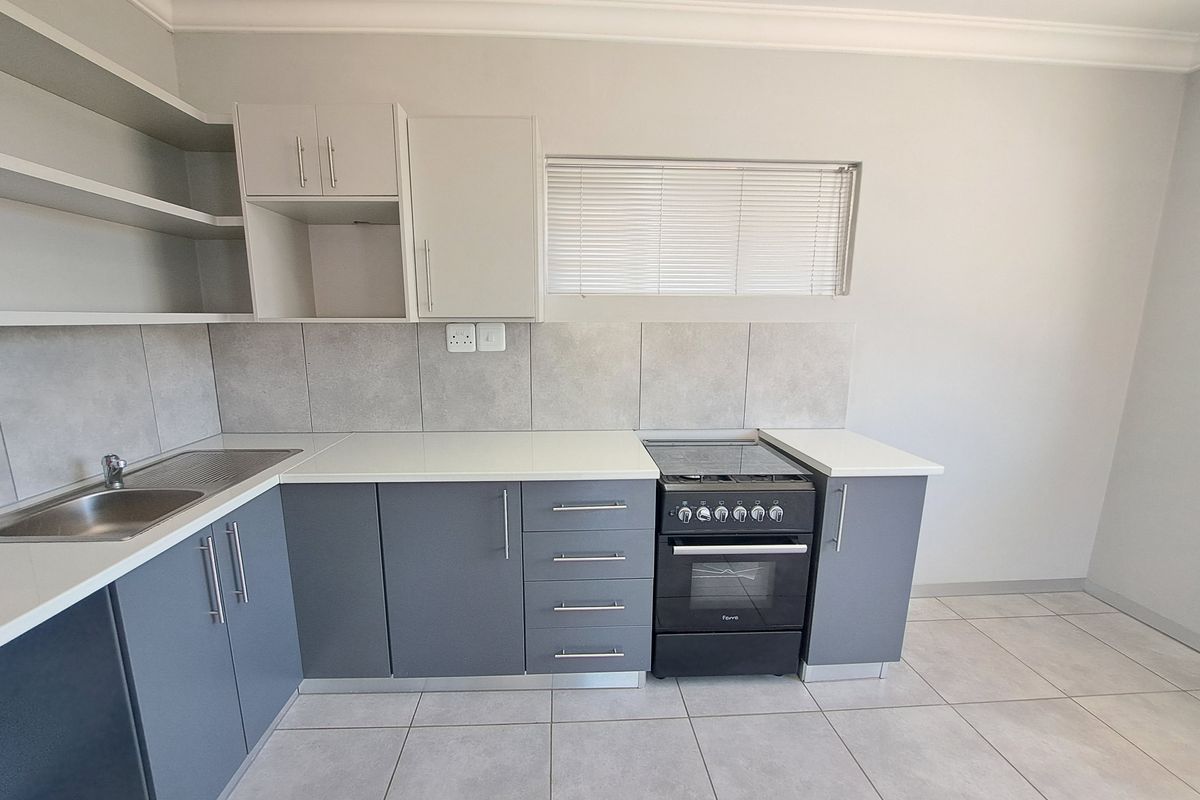 A clean, modern kitchen featuring grey and white cabinetry, stone countertops, tiled backsplash, and a built-in oven with hob.