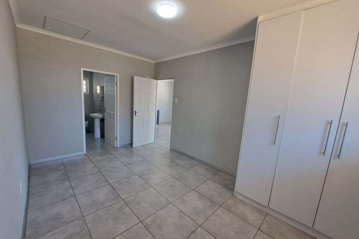A clean, empty bedroom featuring neutral tiled flooring, built-in white cupboards, and direct access to an en-suite bathroom.