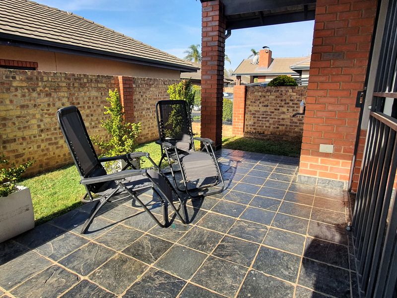 A covered patio area featuring dark tiled flooring, brick support pillars, and a private garden space enclosed by a brick boundary wall.