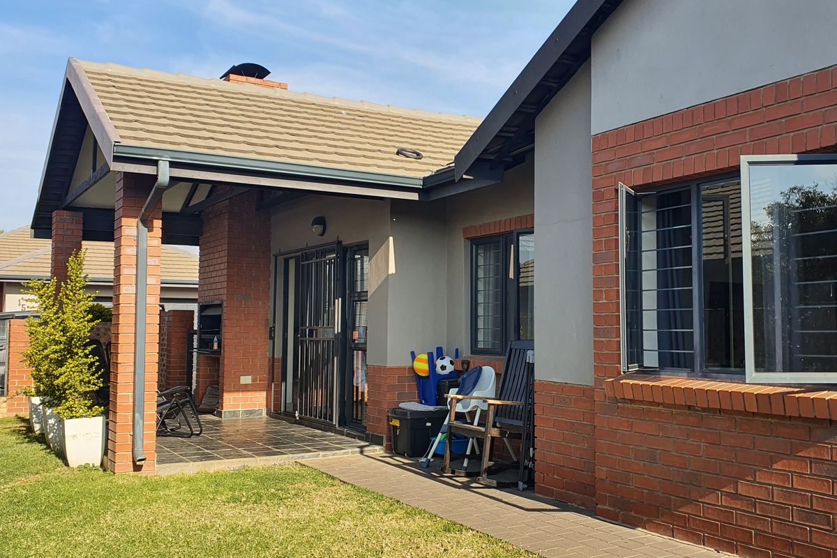 Rear view of the townhouse featuring a covered patio with a built-in braai, brick and plaster facade, and a well-maintained garden area.