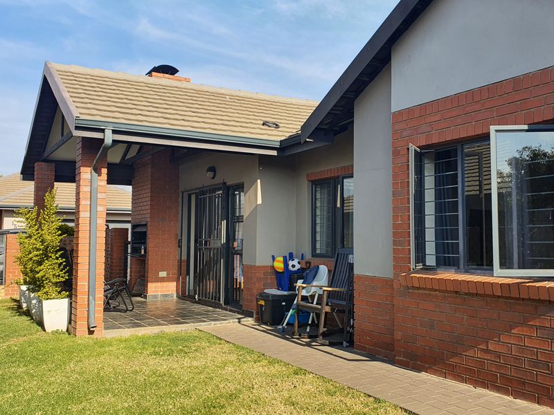 Rear view of the townhouse featuring a covered patio with a built-in braai, brick and plaster facade, and a well-maintained garden area.
