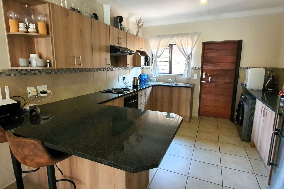 Functional kitchen featuring wood-finish cabinetry, granite countertops, a mosaic tile backsplash, and tiled flooring with an integrated breakfast bar area.