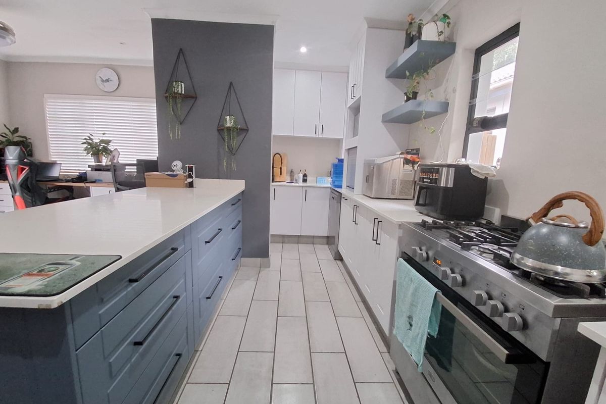 Modern kitchen featuring a large central island, gas stove, ample built-in cabinetry, and stone countertops with tiled flooring throughout.