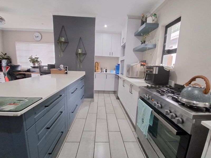Modern kitchen featuring a large central island, gas stove, ample built-in cabinetry, and stone countertops with tiled flooring throughout.