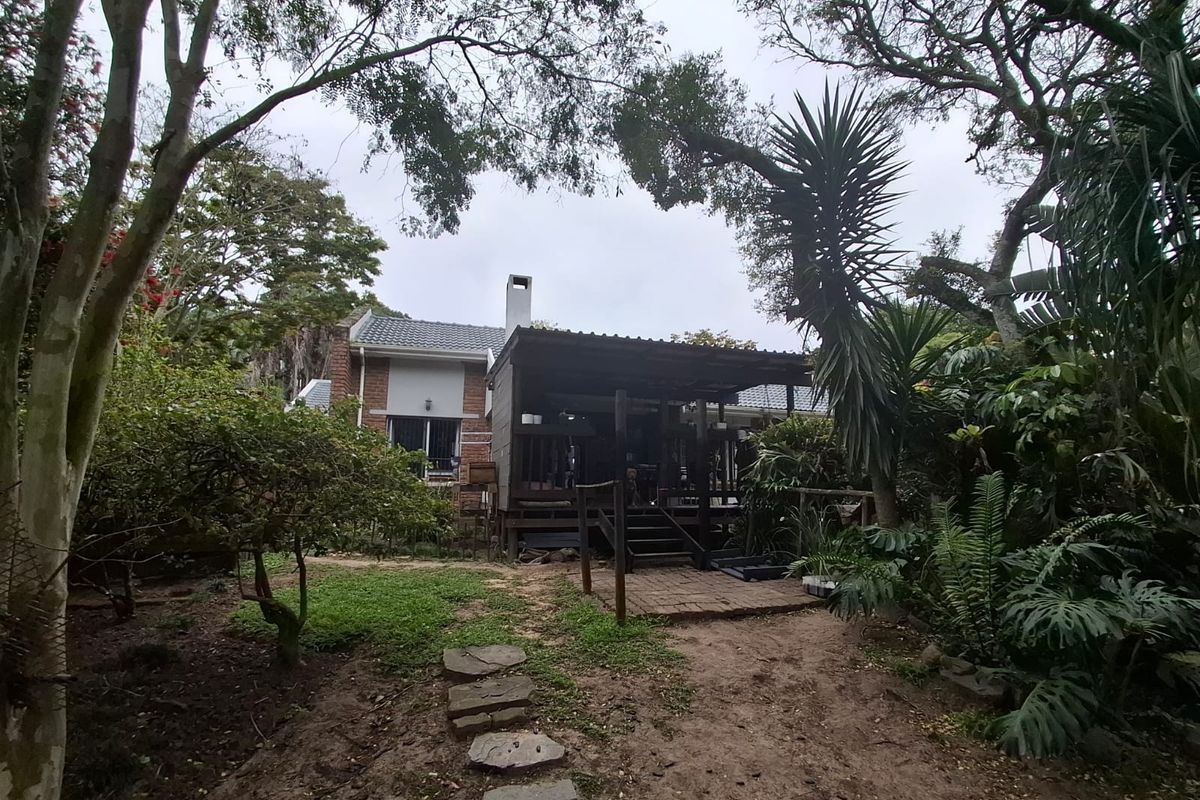 Rear view of the property featuring a timber deck, covered patio area, and established garden with mature trees.