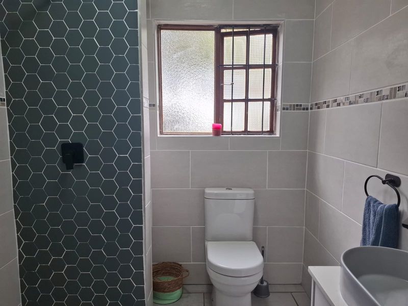 A modern bathroom featuring a striking hexagonal tiled shower wall, neutral ceramic wall tiles, a white toilet, and a contemporary basin.