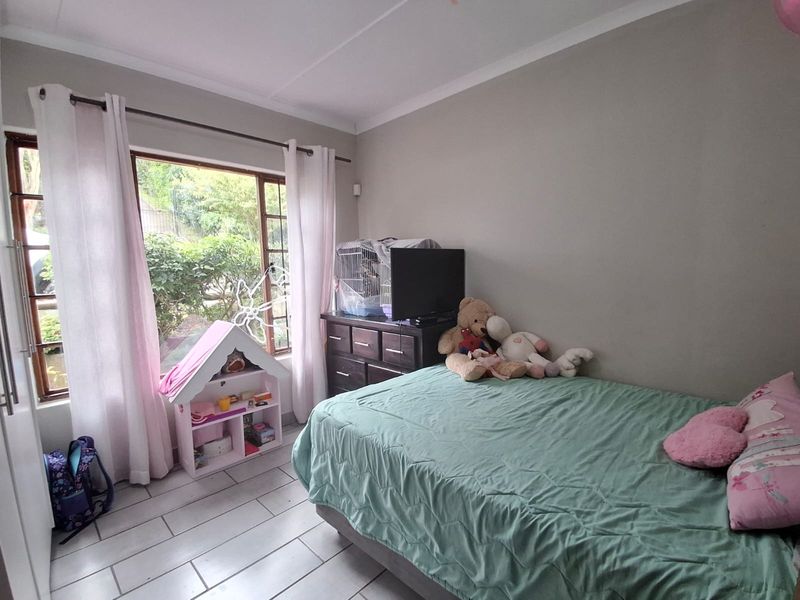 A functional bedroom featuring tiled flooring, neutral wall tones, and a large window providing natural light and garden views.
