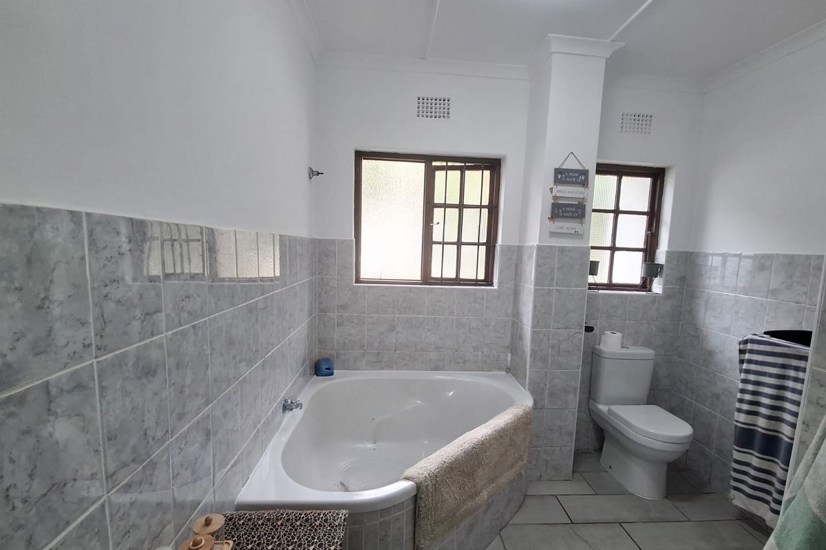 A functional bathroom featuring a corner bathtub, tiled wall finishes, and a standard toilet, with natural light provided by two windows.