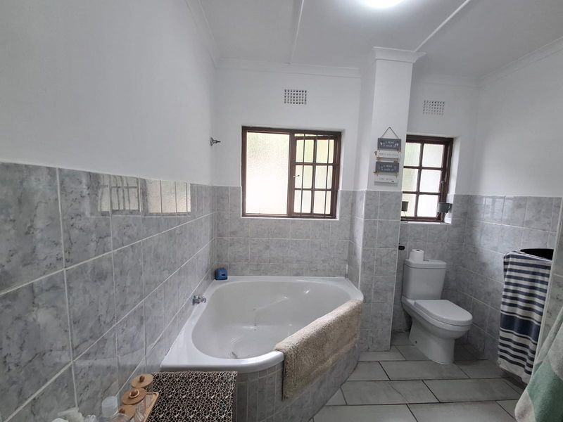 A functional bathroom featuring a corner bathtub, tiled wall finishes, and a standard toilet, with natural light provided by two windows.
