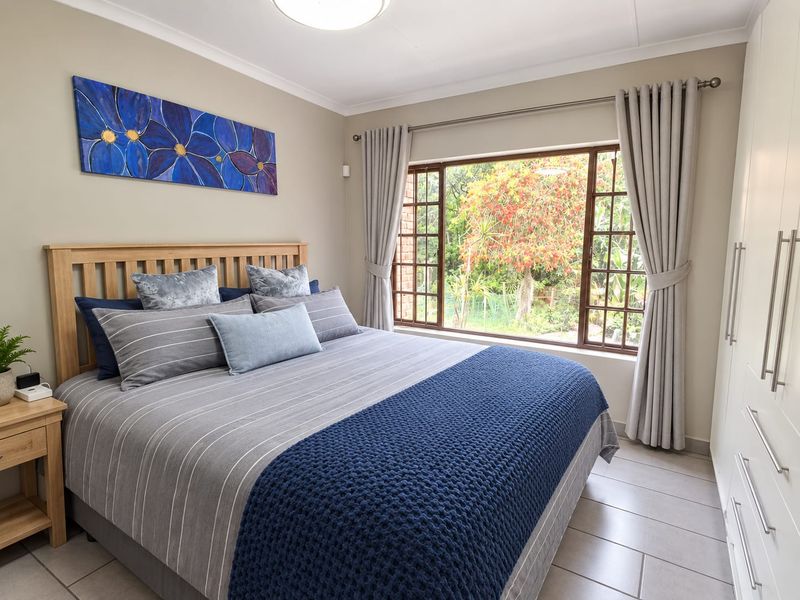 A well-maintained bedroom featuring neutral wall tones, tiled flooring, and ample built-in cupboard storage with a pleasant garden view.