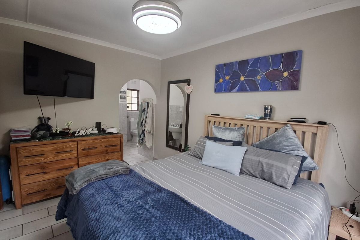 A bedroom featuring tiled flooring, a ceiling fan, and an arched doorway leading to an en-suite bathroom.