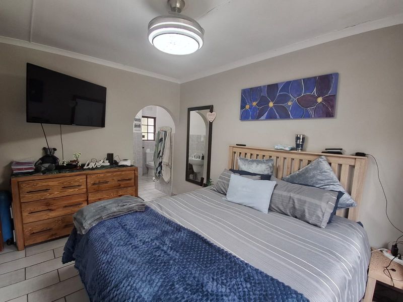 A bedroom featuring tiled flooring, a ceiling fan, and an arched doorway leading to an en-suite bathroom.