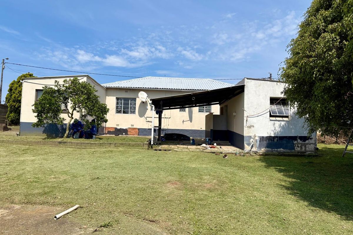 Rear view of a single-story house featuring a covered patio area, corrugated metal roofing, and a large backyard lawn.