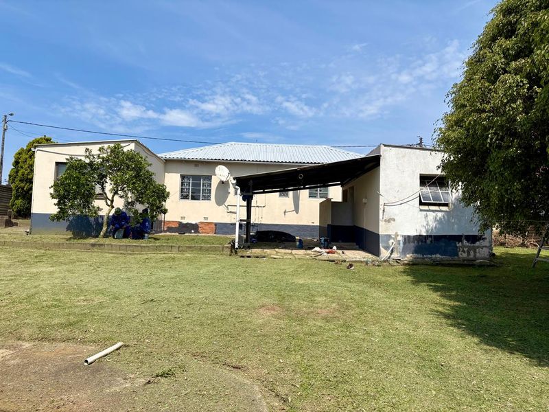 Rear view of a single-story house featuring a covered patio area, corrugated metal roofing, and a large backyard lawn.