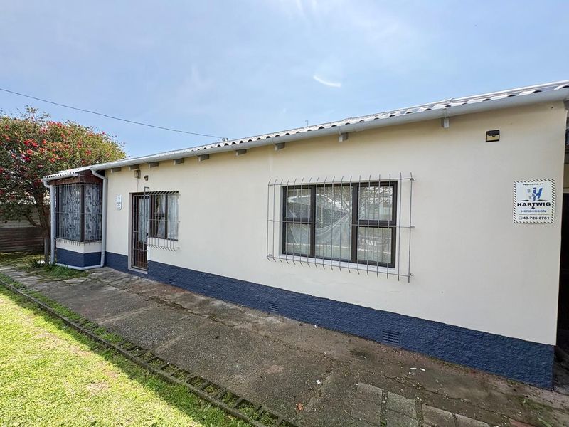 Rear exterior view of the house featuring a concrete pathway, security bars on windows, and painted exterior walls.