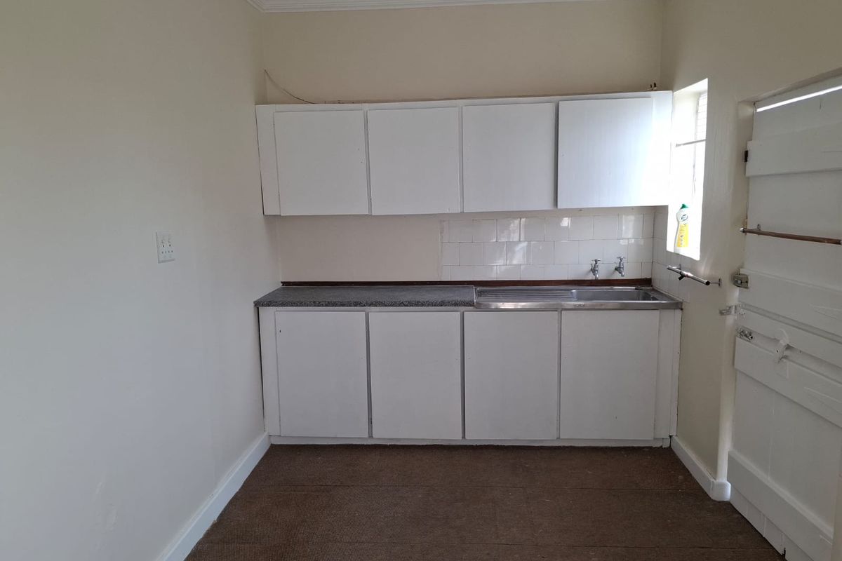 A compact, empty kitchen area featuring basic white cabinetry, a stainless steel sink, and a tiled splashback, offering potential for modernization.