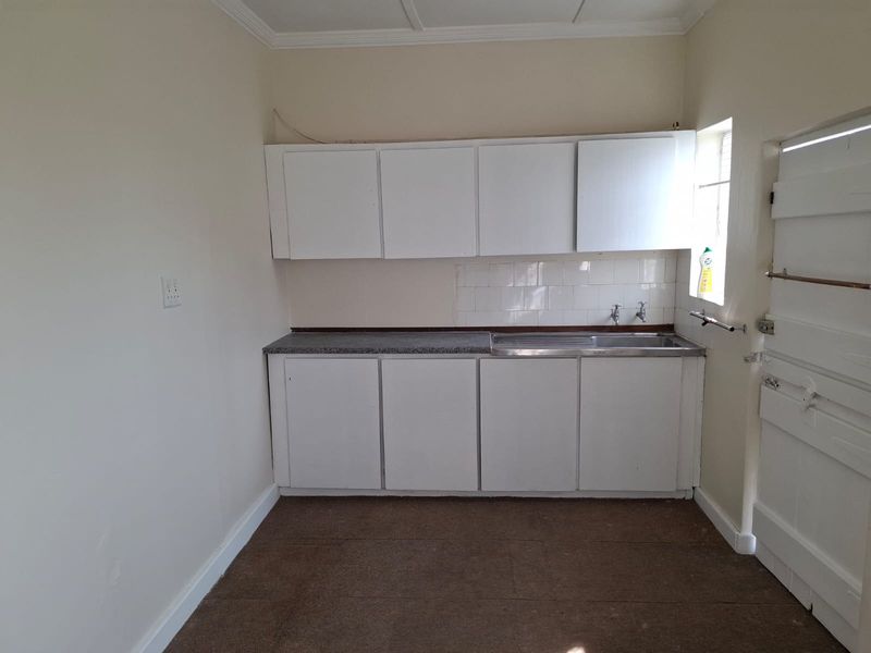 A compact, empty kitchen area featuring basic white cabinetry, a stainless steel sink, and a tiled splashback, offering potential for modernization.