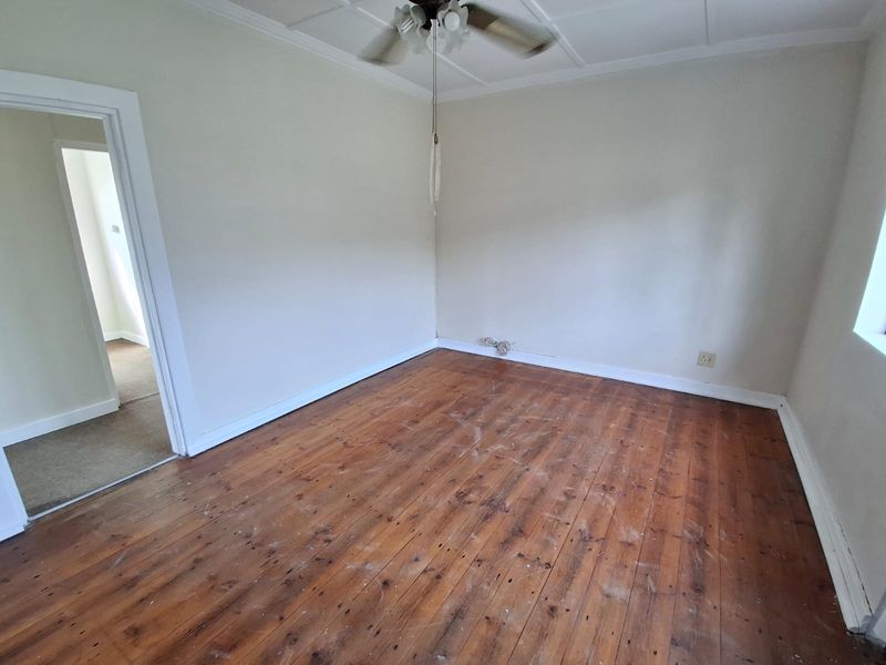 An empty bedroom featuring original hardwood flooring, a ceiling fan, and neutral wall finishes, offering a blank canvas for renovation or staging.