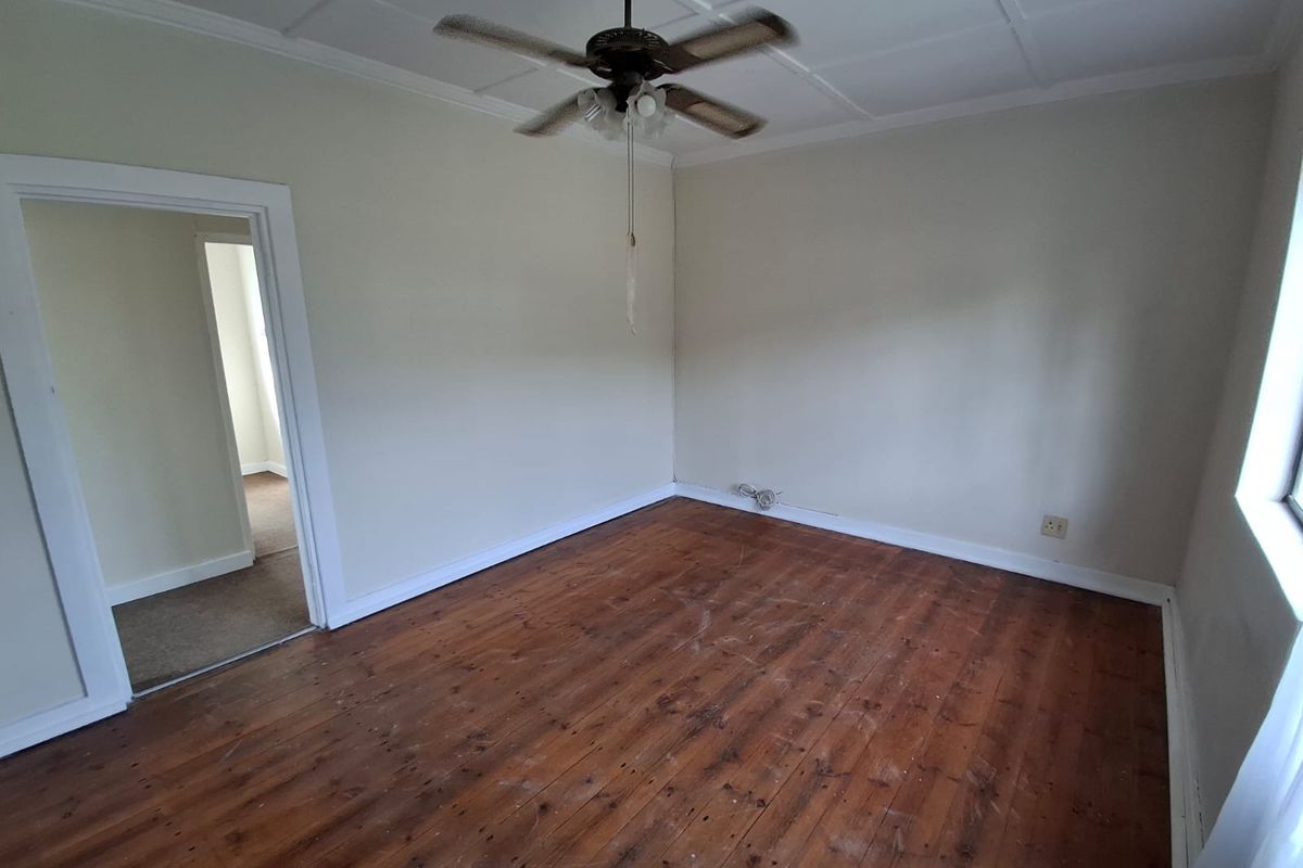 An empty bedroom featuring original hardwood flooring, a ceiling fan, and a tiled ceiling, offering a blank canvas for renovation or interior design.