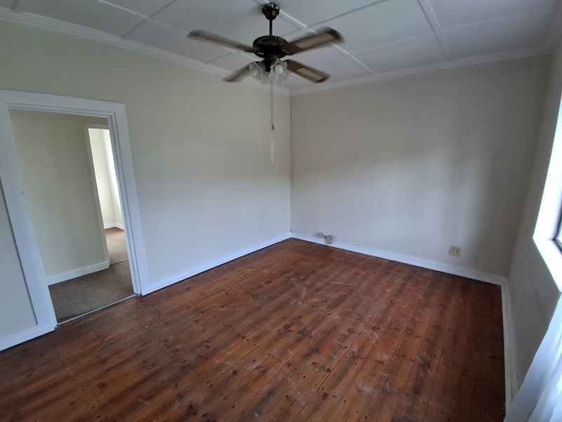 An empty bedroom featuring original hardwood flooring, a ceiling fan, and a tiled ceiling, offering a blank canvas for renovation or interior design.