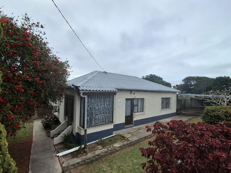 Front view of a single-story house featuring a corrugated metal roof, security bars on windows, and a surrounding concrete pathway.