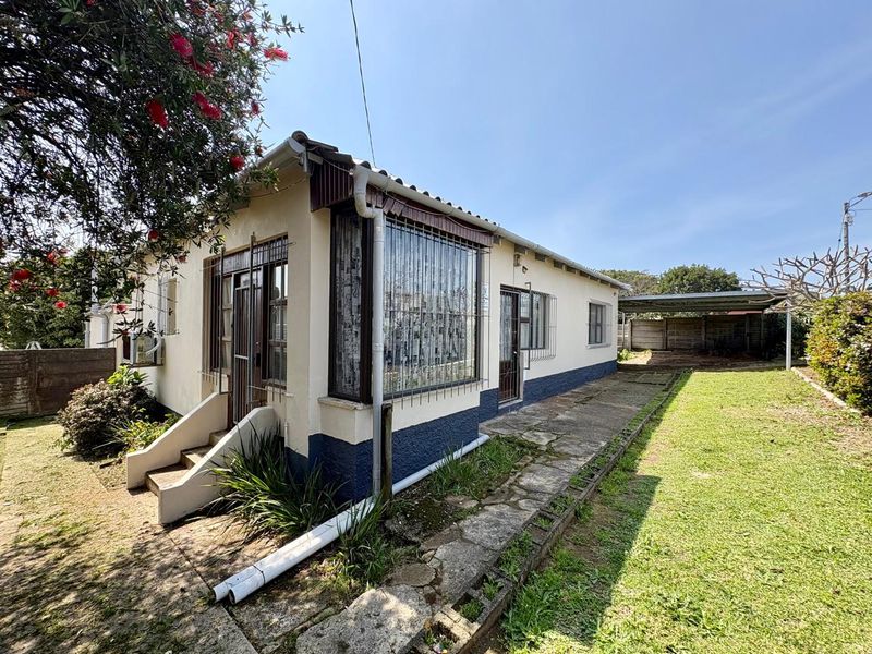 Rear view of the property featuring a concrete pathway, security bars on windows, and a detached carport structure in the backyard.