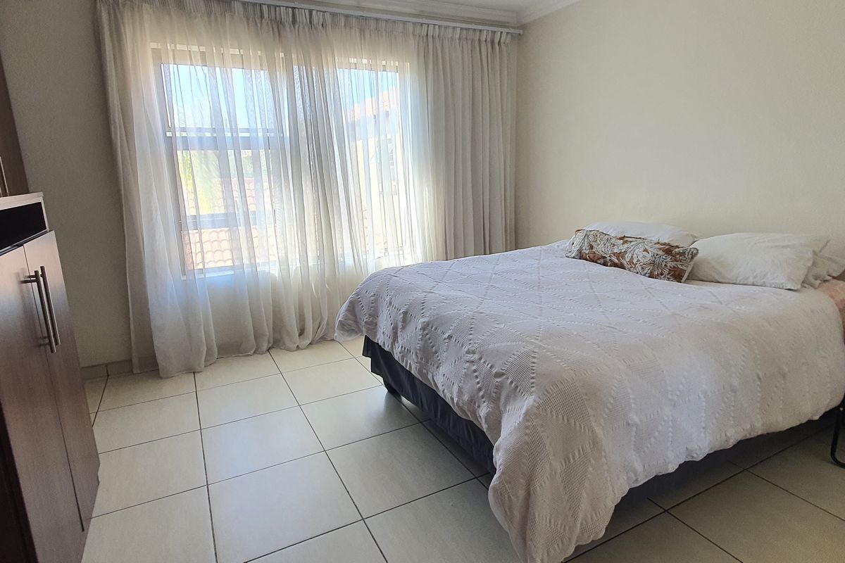 A well-maintained bedroom featuring neutral tiled flooring, built-in cupboards, and large windows with curtain rails allowing for natural light.