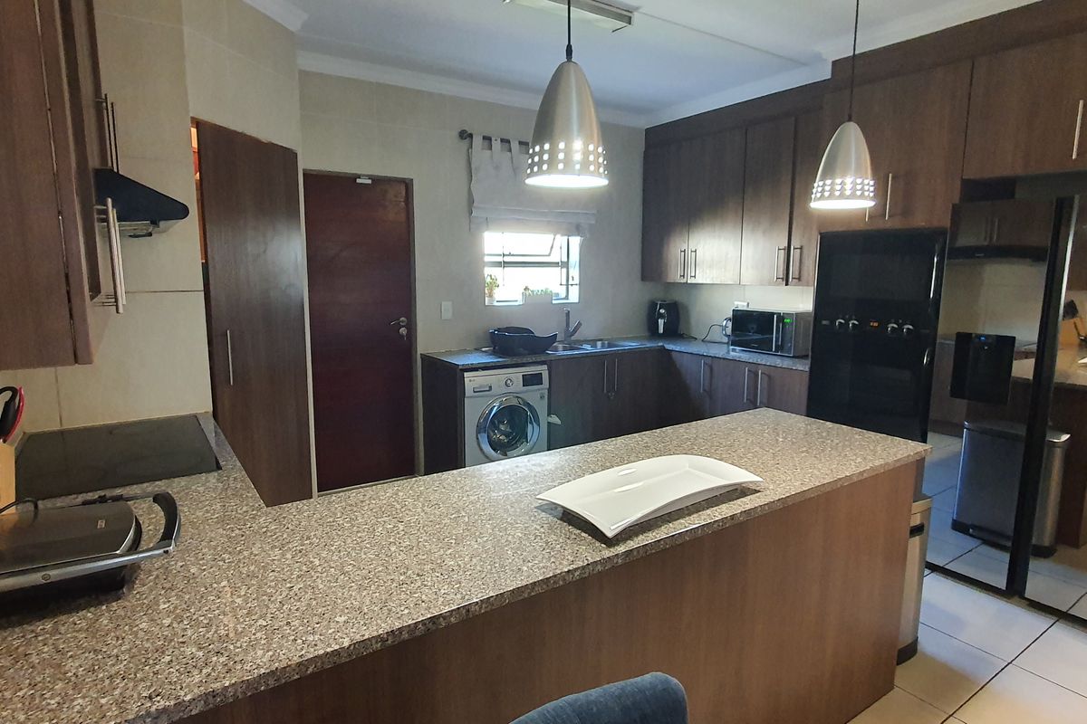 A functional kitchen featuring dark wood cabinetry, granite countertops, integrated appliances, and a breakfast bar, with an adjacent scullery area visible through mirrored doors.