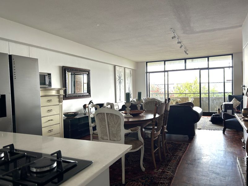 Open-plan living and dining area featuring parquet flooring, track lighting, and large sliding glass doors leading to a balcony.