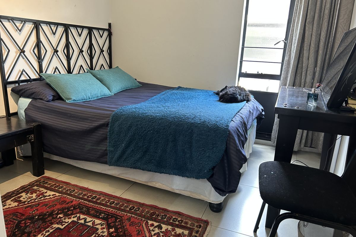 A functional bedroom featuring tiled flooring and a window fitted with security bars, providing natural light and ventilation.