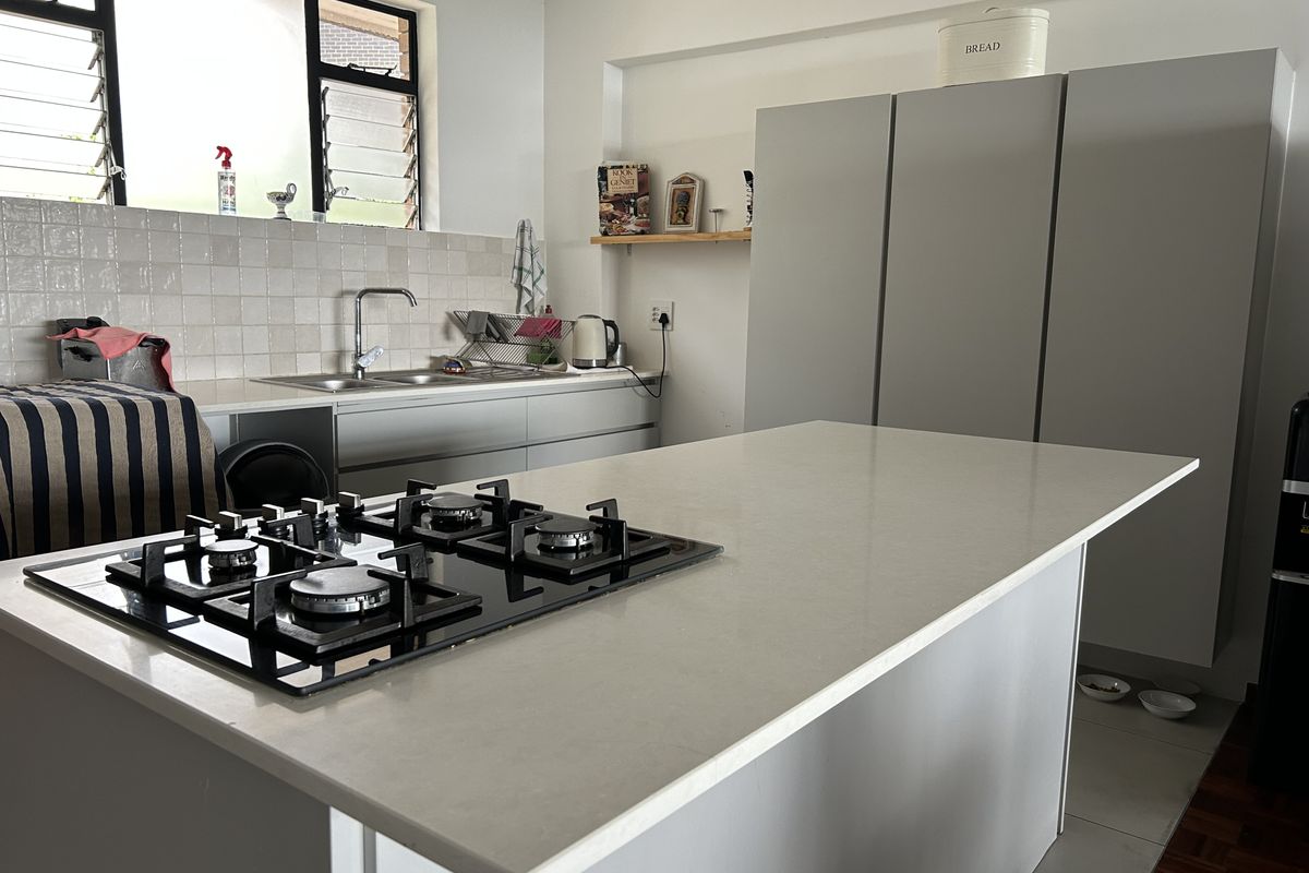 Modern kitchen featuring a central island with a built-in gas hob, ample cabinetry, and a tiled backsplash with a stainless steel sink.