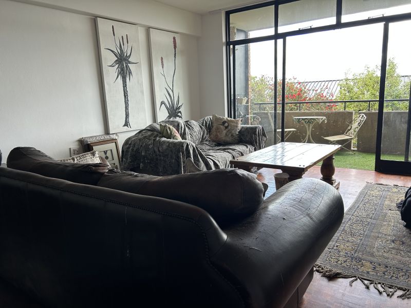Spacious living room featuring classic parquet flooring and large sliding glass doors that provide seamless access to an outdoor balcony area.