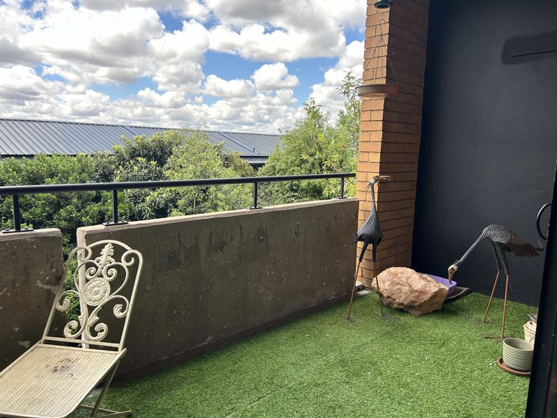 A private balcony featuring a brick pillar, metal railing, and artificial turf flooring, offering an outdoor space with a view.